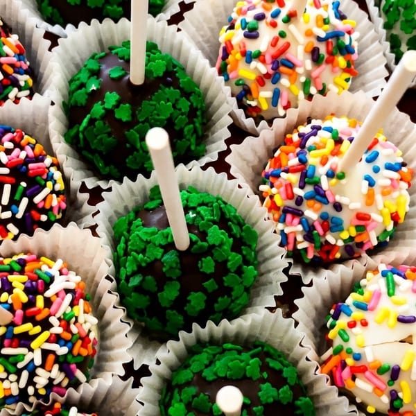 Variety of chocolate and white cake pops with colorful and green clover sprinkles.