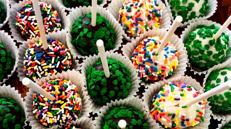 Assortment of chocolate and white cake pops with colorful sprinkles and green leaf toppings.