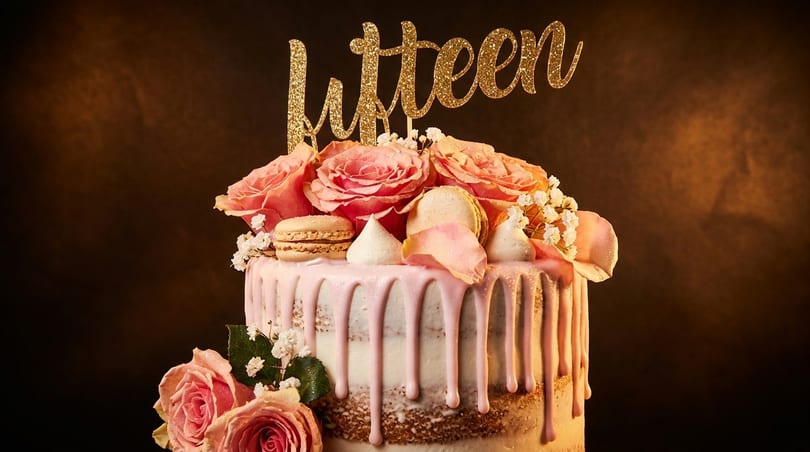 Pink drip cake with fresh roses, macarons, meringue, and a glitter "fifteen" topper.